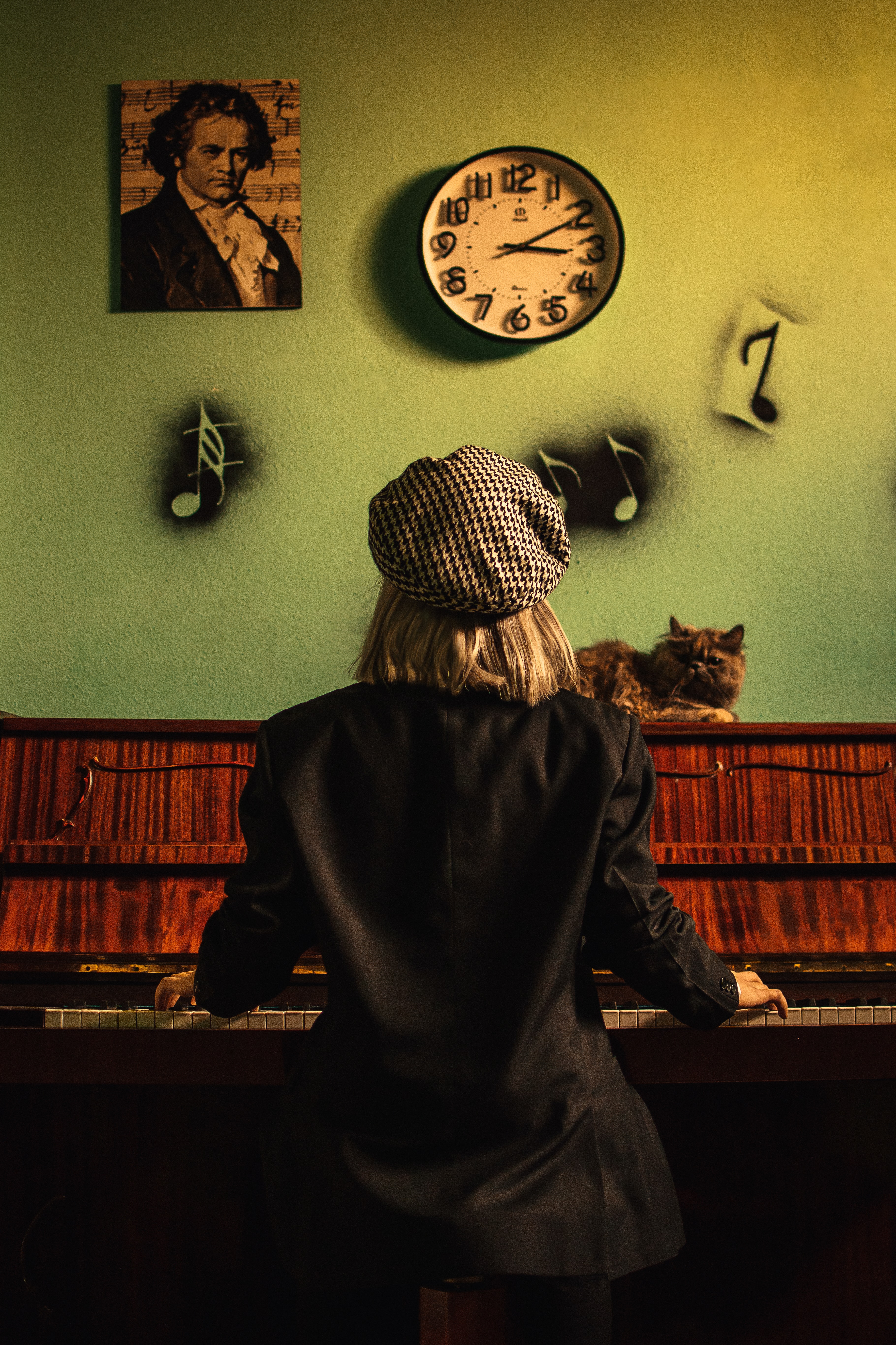 Woman playing piano in front of a green painted wall.